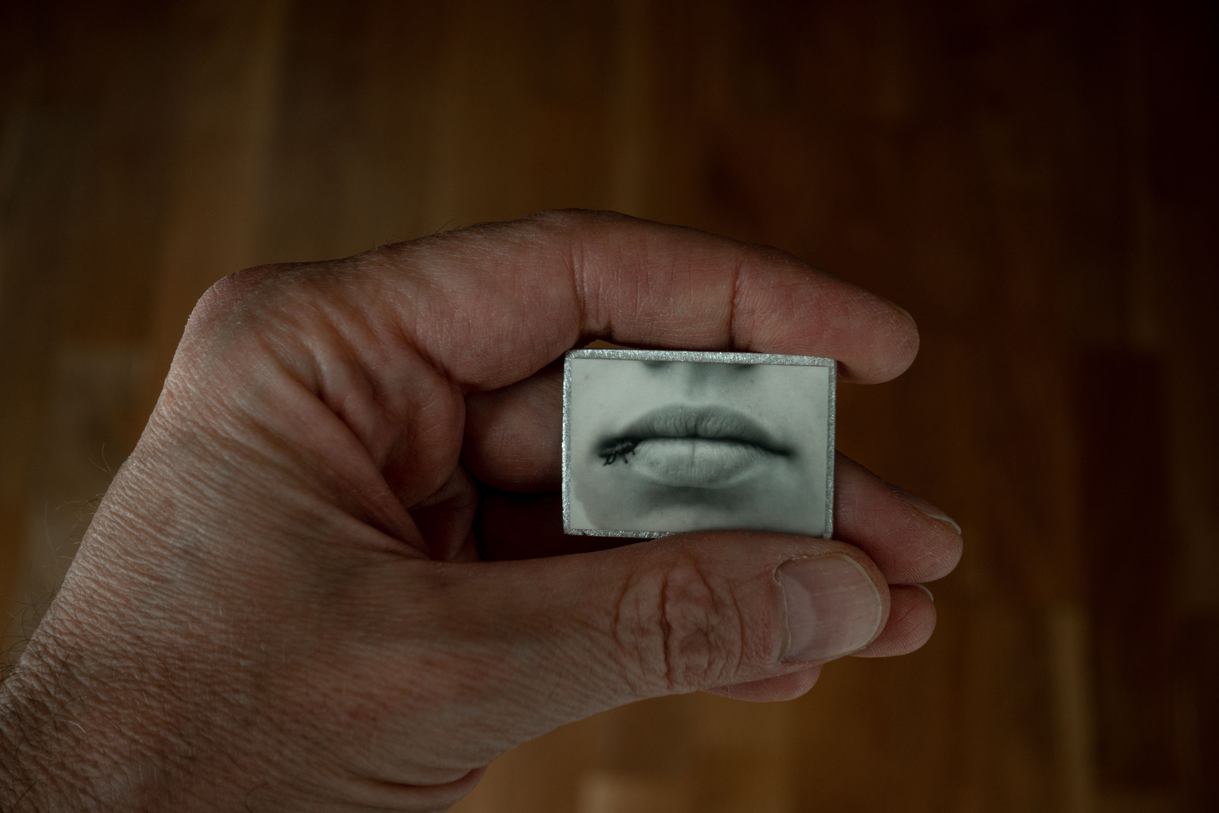 Hand holding a small black and white photograph of a woman's lips with an ant on them.