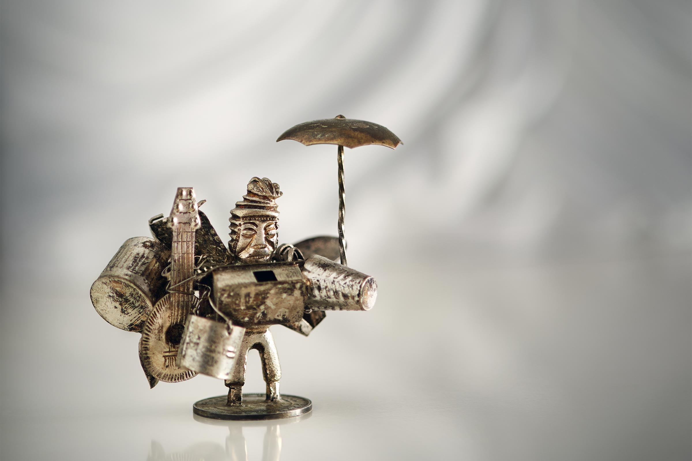 Miniature metallic sculpture of a street musician set against a white background.