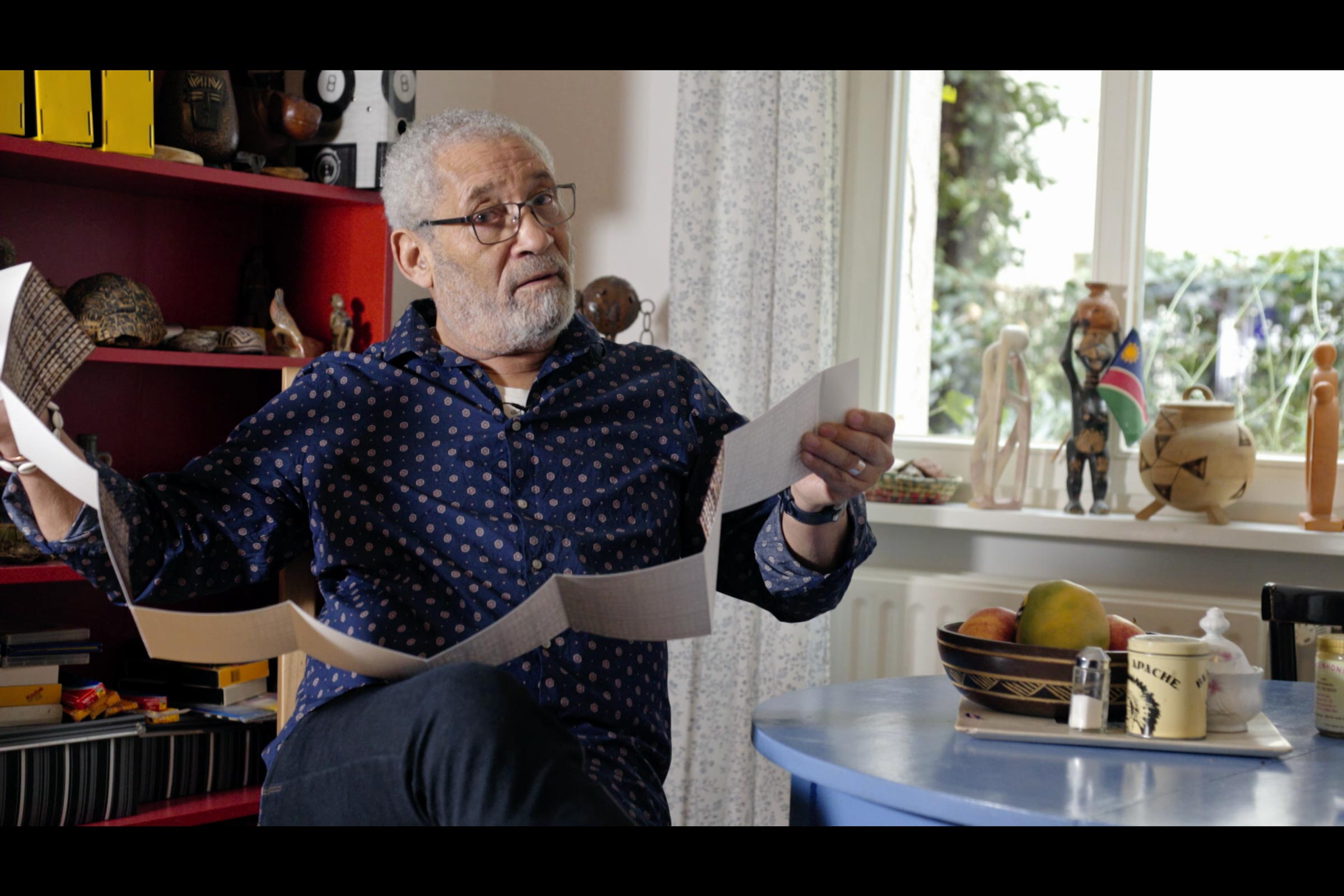 A man sitting, holding a long collapsible print with both hands, looking at the camera.