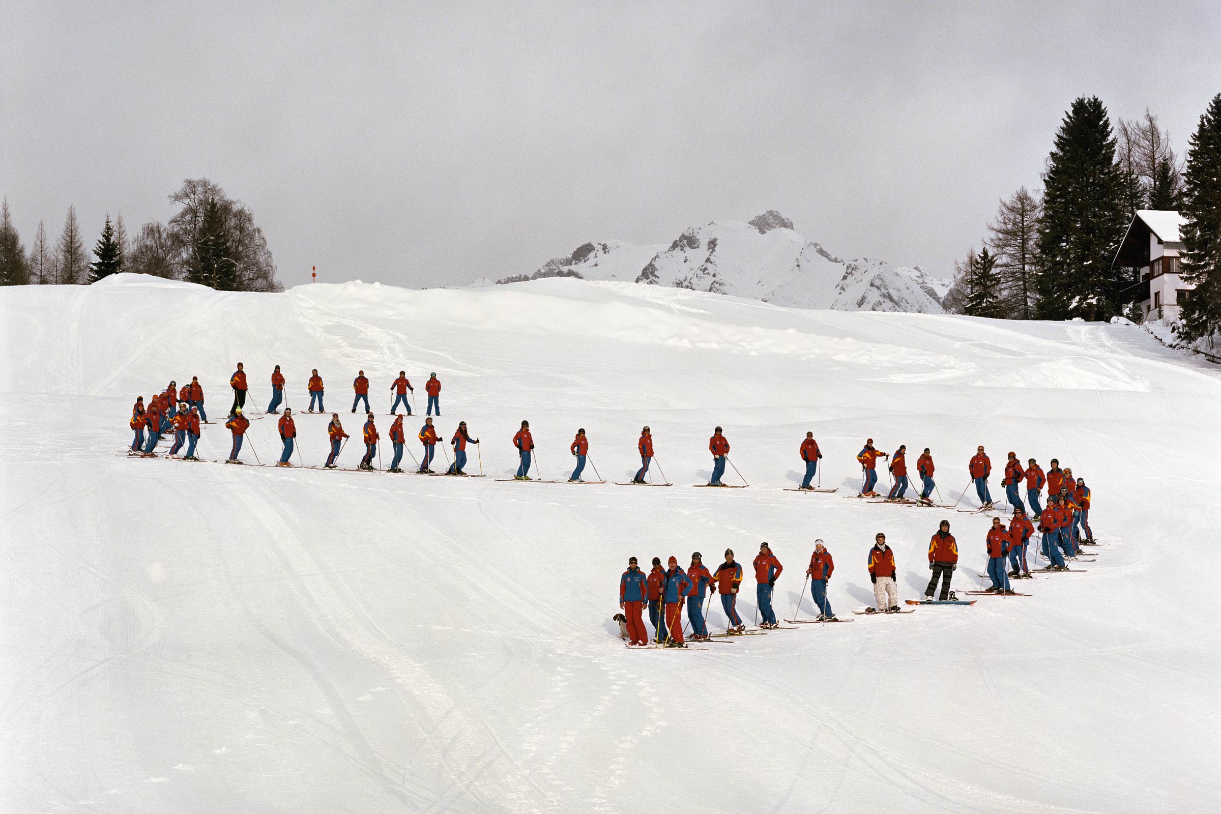 A group of skiers with red jackets organized on a ski slop in a curved S formation