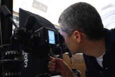 Man looking through a viewfinder of a digital camera in front of shelves with skulls on them