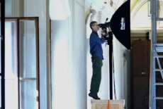 Man standing on his tiptoes on a box looking through a camera