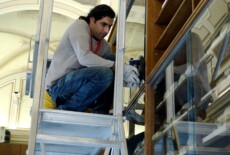 Man on scaffolding handling a glass door in a wooden cabinet