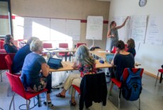 The Dead Images team (CCP 4) during a workshop on education with Karin Schneider and Nora Landkammer, Vienna, 2016. Group of people sitting in a seminar room with large handwritten sheets covering the walls; one woman stands next to one of the sheets.