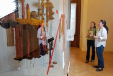 Sharon Macdonald visiting the new exhibition at the Weltmuseum Wien with museum curator Claudia Augustat, 2017. Two women standing in front of a museum display behind glass doors.