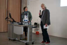 Anna Szöke and John Harries speaking at the Dead Images Conference, Edinburgh College of Art, July 2018. Woman and man standing and talking to an audience in an event hall.