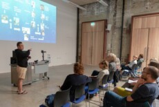 Te Herekiekie Herewini speaking at the Dead Images Conference, Edinburgh College of Art, July 2018. Man standing and talking to an audience in an event hall.