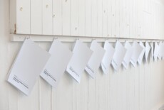White brochures hanging from hooks in a white wall in an exhibition space