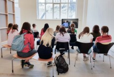 Group of students watching the video PHOTOGRAPH at the Dead Images exhibition, Edinburgh College of Art, July 2018. Group of students sitting at an exhibition space and looking at a monitor with a video playing.