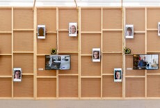 Wooden wall with several video monitors mounted on it and playing different videos at an exhibition space.