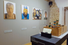 Installation view, Terribly Close exhibition, The Ethnographic Museum in Kraków, 2018-2019. Exhibition space with images on the wall and a table with small figurines inside a glass box and some cards.