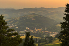The town of Predappio with the former House of the Fascist Party at the centre. Image captured from the Rocca delle Caminate, 2025. Landscape scene in evening sunset colors. In the distance, a small village in a valley surrounded by mountains.