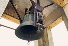 Original bronze bell installed in the tower of the former House of the Fascist Party. Predappio, Italy, 2025. Bronze bell hanging from a rusty metal structure, shot from below.