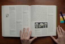 Two hands holding an open book; the right-hand page shows three photographs of a skull.