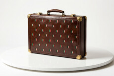 Still from an AI-generated sequence in Fragile Power, 2026. Leather briefcase with all-over Italian flag pattern displayed on a white circular platform. AI generated.