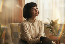 Still from an AI-generated sequence in Fragile Power, 2026. Woman in a 70s style room looking upwards with a small smile. AI generated.